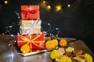 Stack of festive gift boxes with red top and gold bottom, tied with ribbons, set against string lights and a dark backdrop.